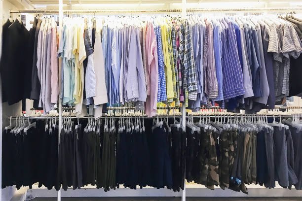 Many new style colorful shirts and black trousers hanging on long stainless rail ready for sale in the clothing store.